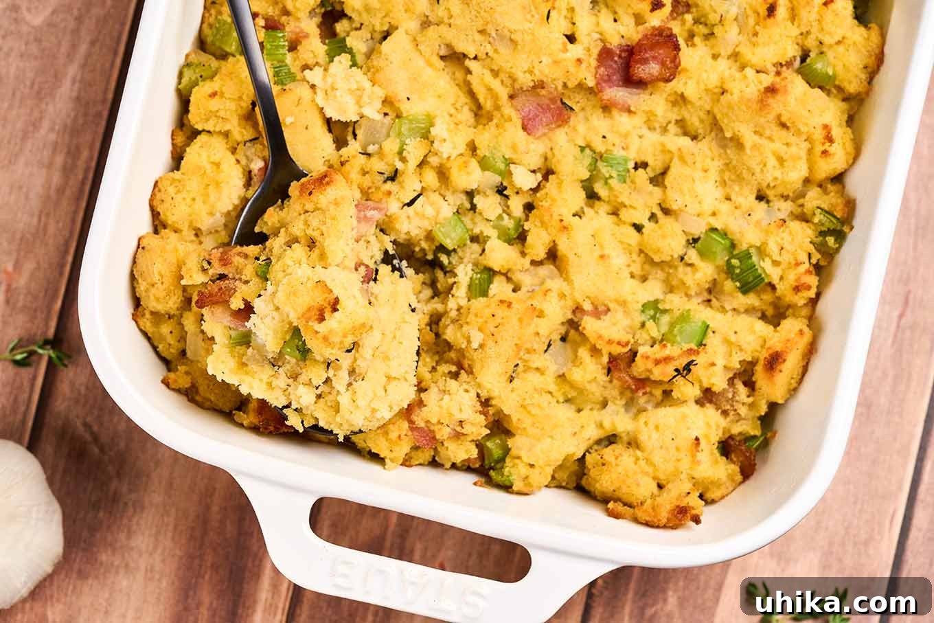 Smoked Bacon Cornbread Dressing 8 A close up of baked cornbread stuffing in a casserole dish, showing bits of bacon, celery, onion, and thyme throughout.