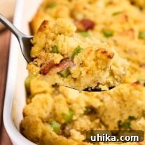 Smoked Bacon Cornbread Dressing 9 A serving of cornbread stuffing with bacon being spooned out of a white casserole dish.