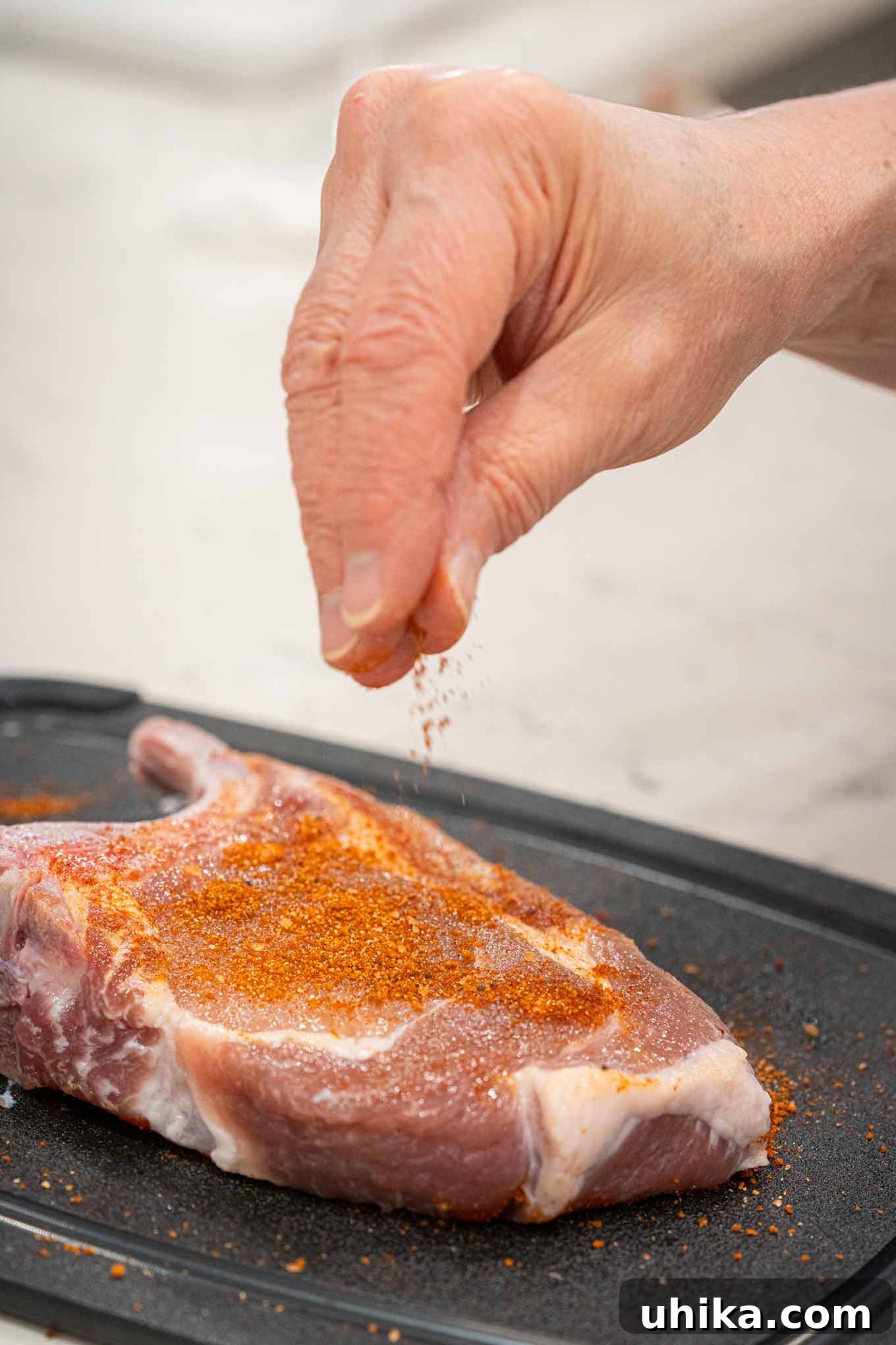 Effortless BBQ Flavor Blend 4 BBQ spice rub being sprinkled onto pork chops showing how to get even distribution of the rub on meat.