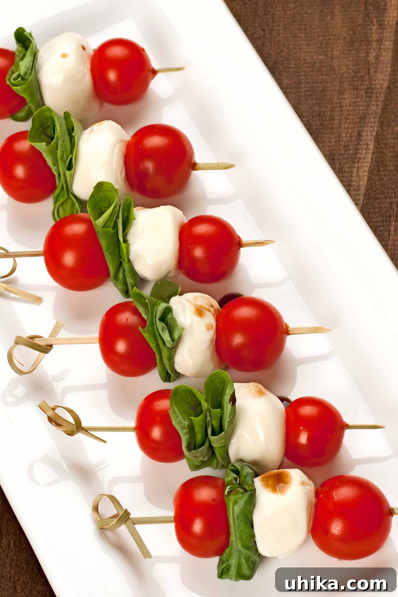 Caprese Party Skewers 2 A vibrant serving platter adorned with numerous Caprese salad skewers. Each skewer features juicy cherry tomatoes, fragrant green basil leaves, and creamy fresh mozzarella balls, artfully arranged and lightly drizzled with balsamic glaze, creating an inviting and colorful appetizer.