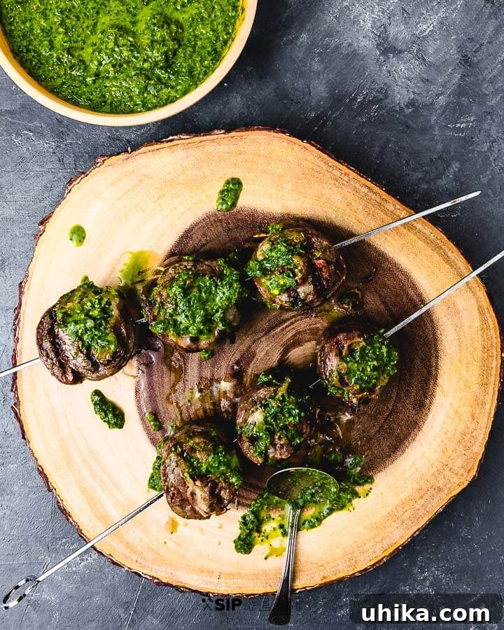 Savory Steak Swirls 2 An overhead shot showcasing two skewers of perfectly grilled beef pinwheels on a wooden cutting board, with a small bowl of green sauce on the side.