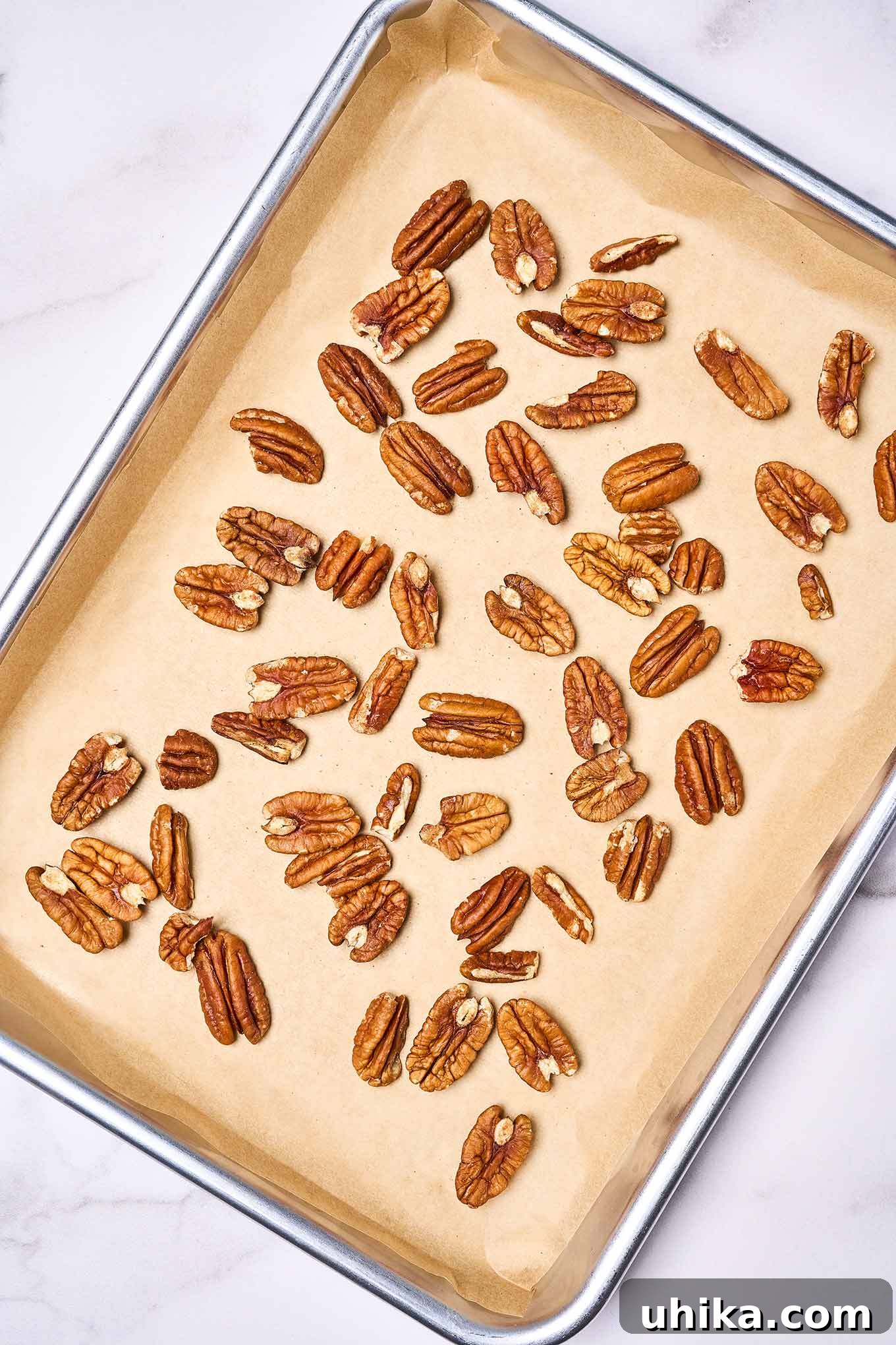 Pecan halves laid out on a parchment lined baking sheet, ready to go into the oven for toasting.