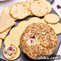 A close up view of a cranberry cheese ball with a portion removed revealing the creamy cheese studded with dried cranberries and fresh orange zest.