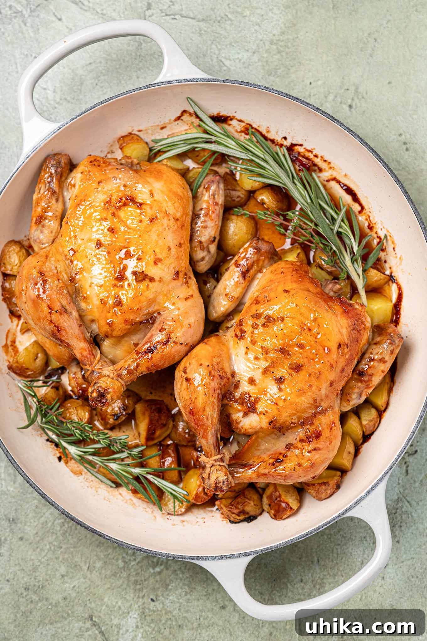 Golden Bourbon Glazed Cornish Hens 2 Two roasted cornish hens glazed with bourbon and honey in an enameled cast iron pan with baby potatoes and a garnish of fresh rosemary and thyme.