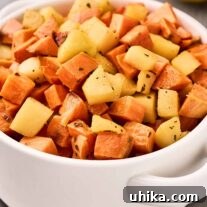 A round white serving dish of roasted sweet potatoes and apple with fresh sage and lemon. Half a lemon and sage leaves in the background.