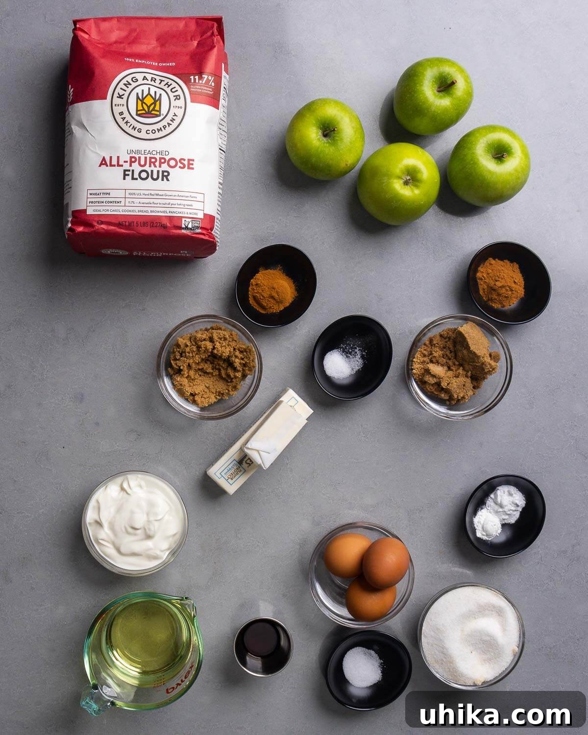 Scrumptious Apple Coffee Cake with Golden Streusel Topping 4 A vibrant display of all the recipe ingredients laid out: flour, fresh apples, ground cinnamon, brown sugar, salt, unsalted butter, sour cream, vegetable oil, vanilla extract, eggs, baking soda, baking powder, and granulated sugar.