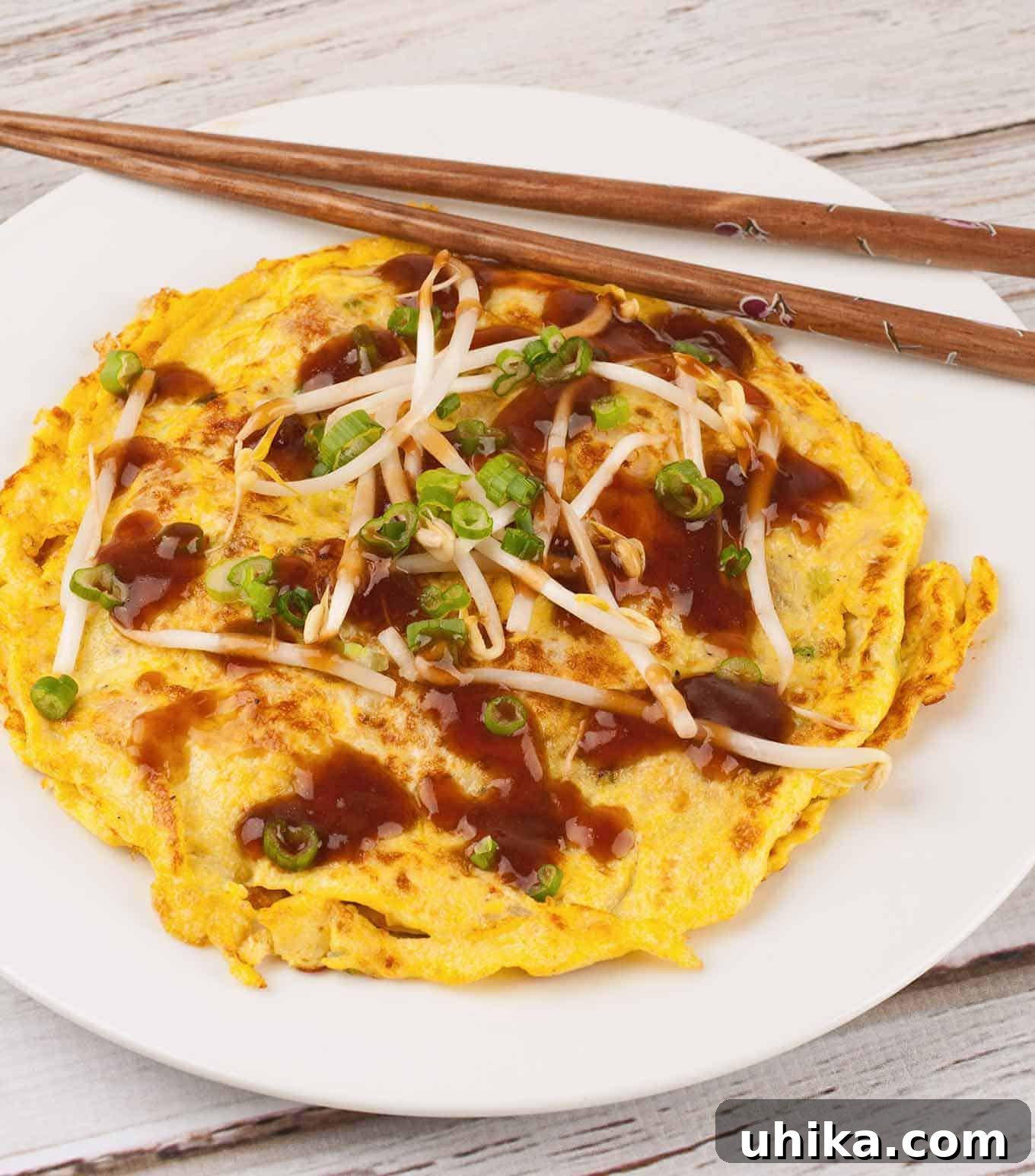 Savory Chinese Egg Patties 2 Golden Egg Foo Young omelet topped with rich brown gravy, crisp bean sprouts, and freshly sliced green onions on a pristine white plate, accompanied by elegant chopsticks.