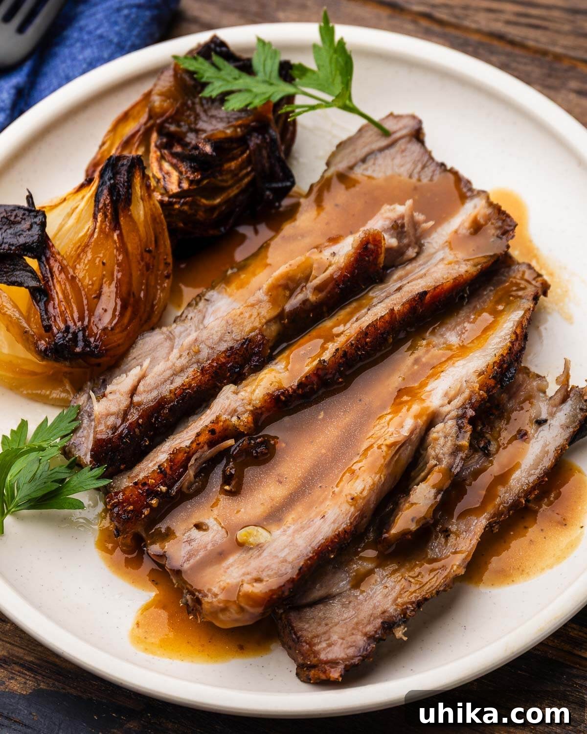 Slow Roasted Tuscan Pork Shoulder 2 White plate with perfectly sliced roasted pork shoulder, garnished with fresh herbs and rich gravy.