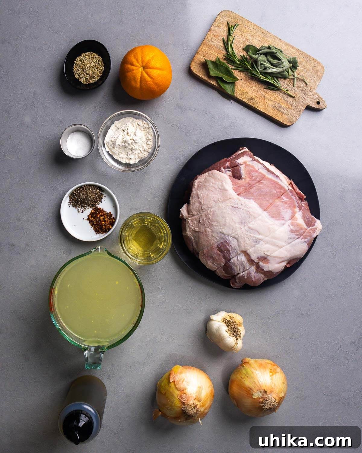 Slow Roasted Tuscan Pork Shoulder 4 A flat lay photograph showcasing all the fresh ingredients needed for the roasted pork shoulder: fennel seeds, an orange, salt, flour, sage, rosemary, black pepper, hot red pepper flakes, white wine, pork shoulder, chicken stock, garlic, olive oil, and onions.