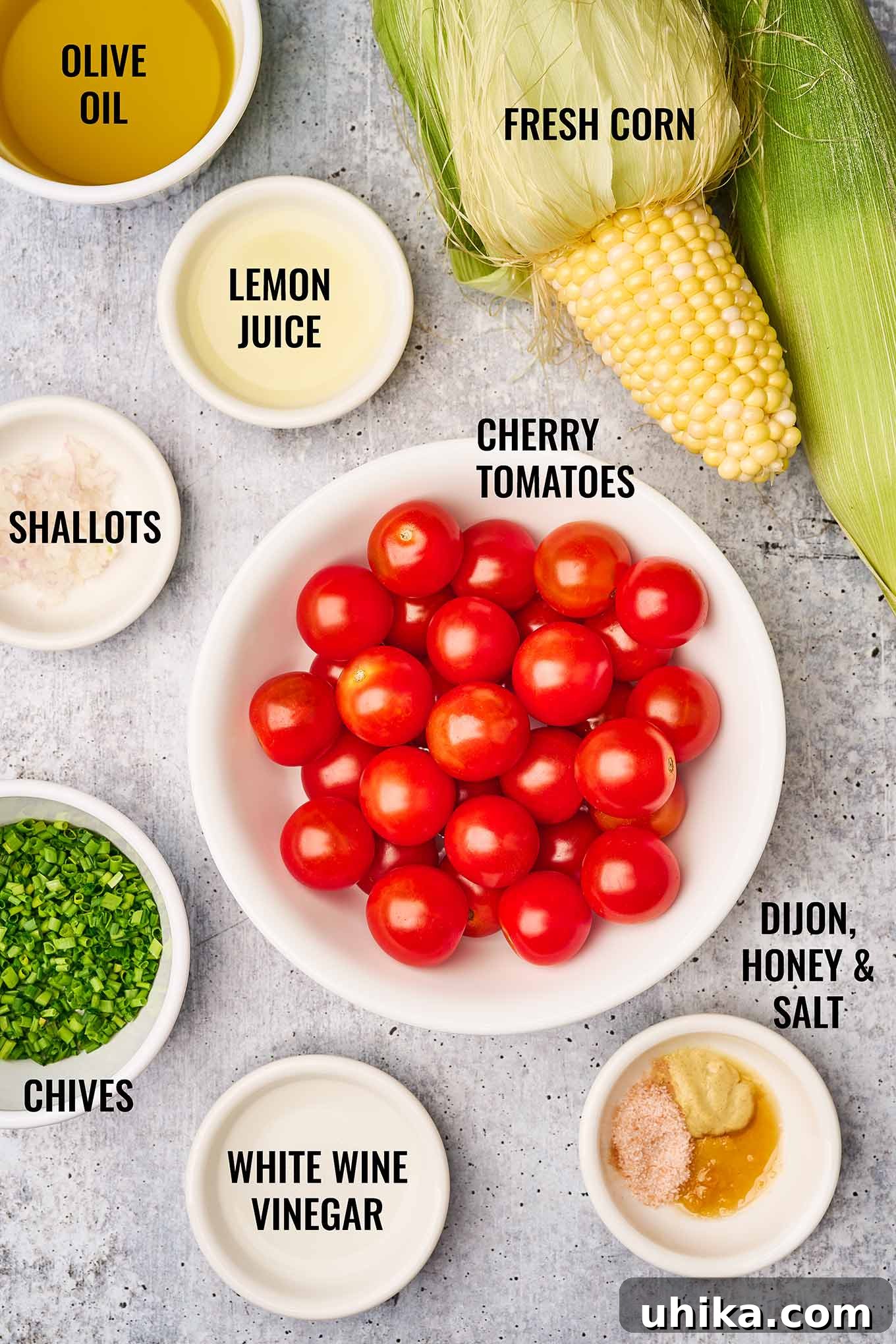 Labeled photo of corn and tomato salad ingredients including cherry tomatoes, fresh corn on the cob, lemon juice, shallots, and chives.