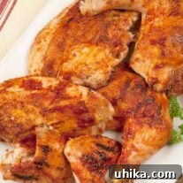 A white serving platter with bbq chicken parts, leg quarters, breasts, and wings. A sprig of parsley on the side and a jar of bbq spice rub in the background.