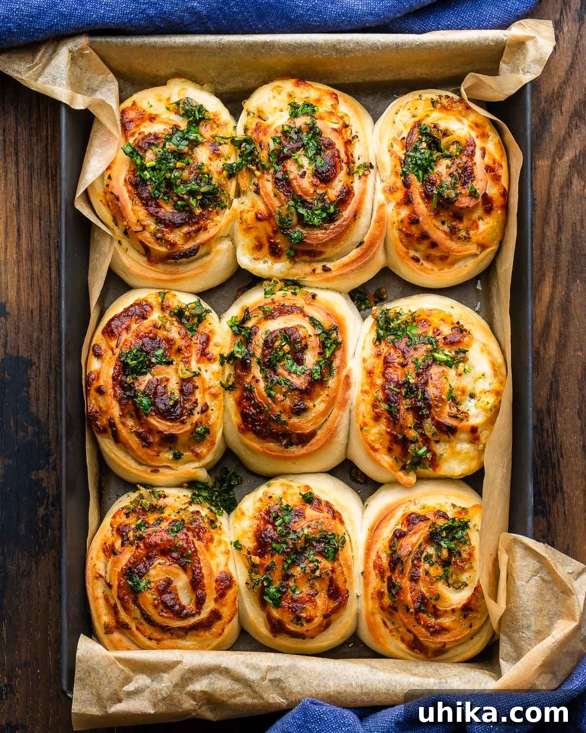 Gooey Garlic Stuffed Cheese Rolls 2 A large grey baking dish brimming with golden-brown, puffy cheesy garlic rolls, freshly baked and glistening with melted cheese and fresh herbs.