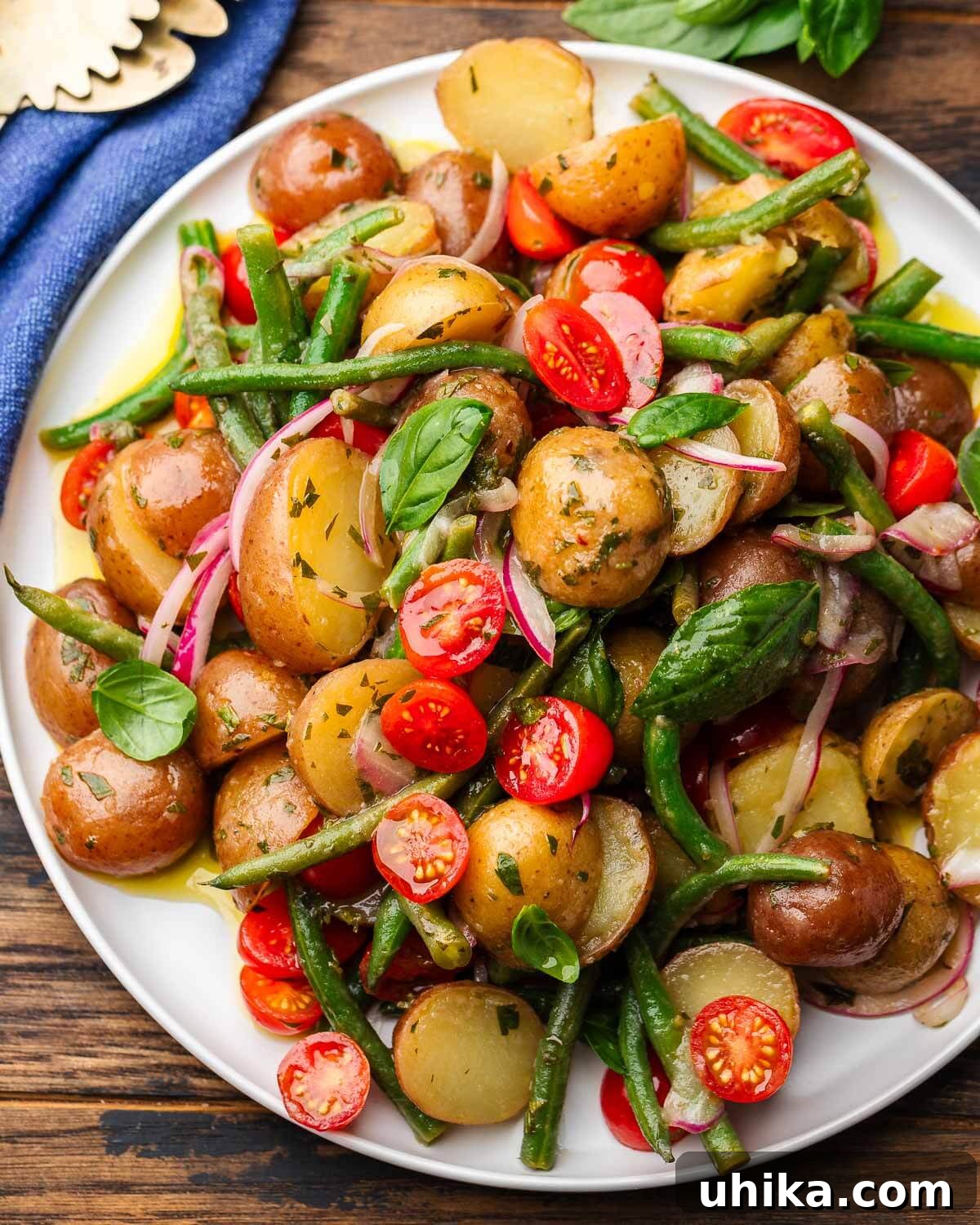 Rustic Italian Potato Salad with Green Beans and Tomatoes 2 A beautifully arranged Italian potato salad featuring warm potatoes, green beans, cherry tomatoes, and red onion on a white platter with a blue napkin.