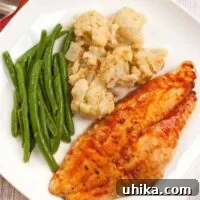 Baked Creole catfish fillet served with roasted cauliflower and steamed green beans on a white plate.