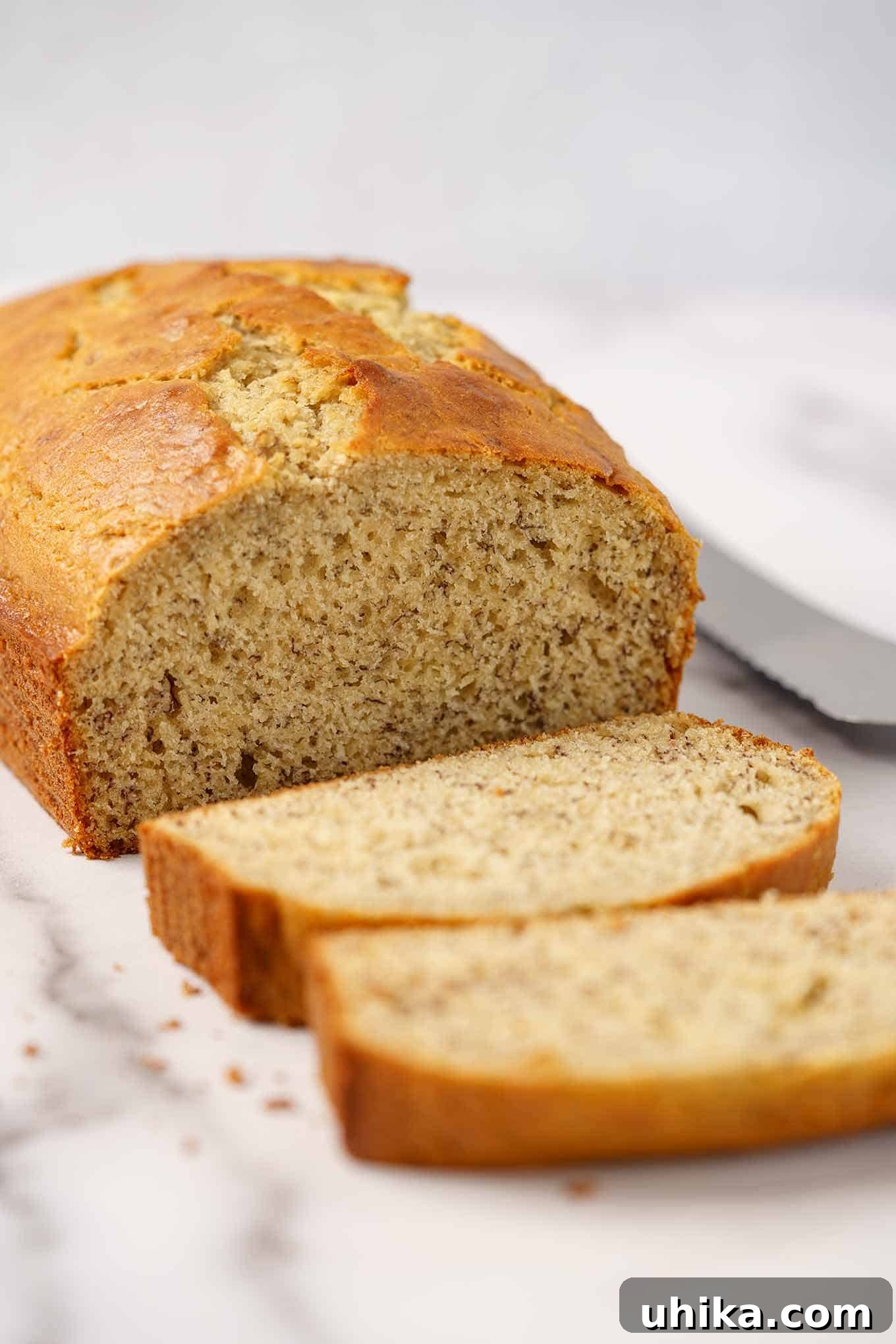 Velvety Sour Cream Banana Bread 2 A partially sliced loaf of sour cream banana bread on a marble board with a bread knife in the background, ready to be enjoyed.