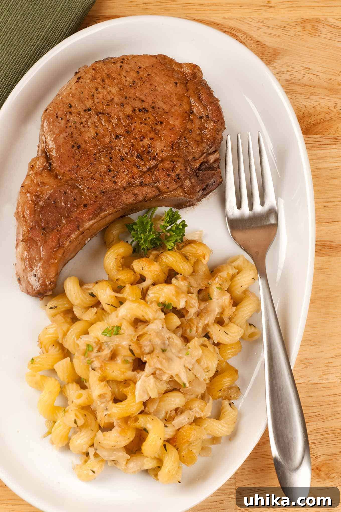 Golden-Seared Pork Rib Chops 2 A pan-seared pork rib chop served with cheesy cavatappi pasta and garnished with parsley on a white plate.