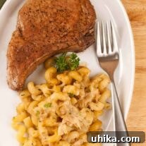 A pan-seared pork rib chop served with cheesy cavatappi pasta and garnished with parsley on a white plate.