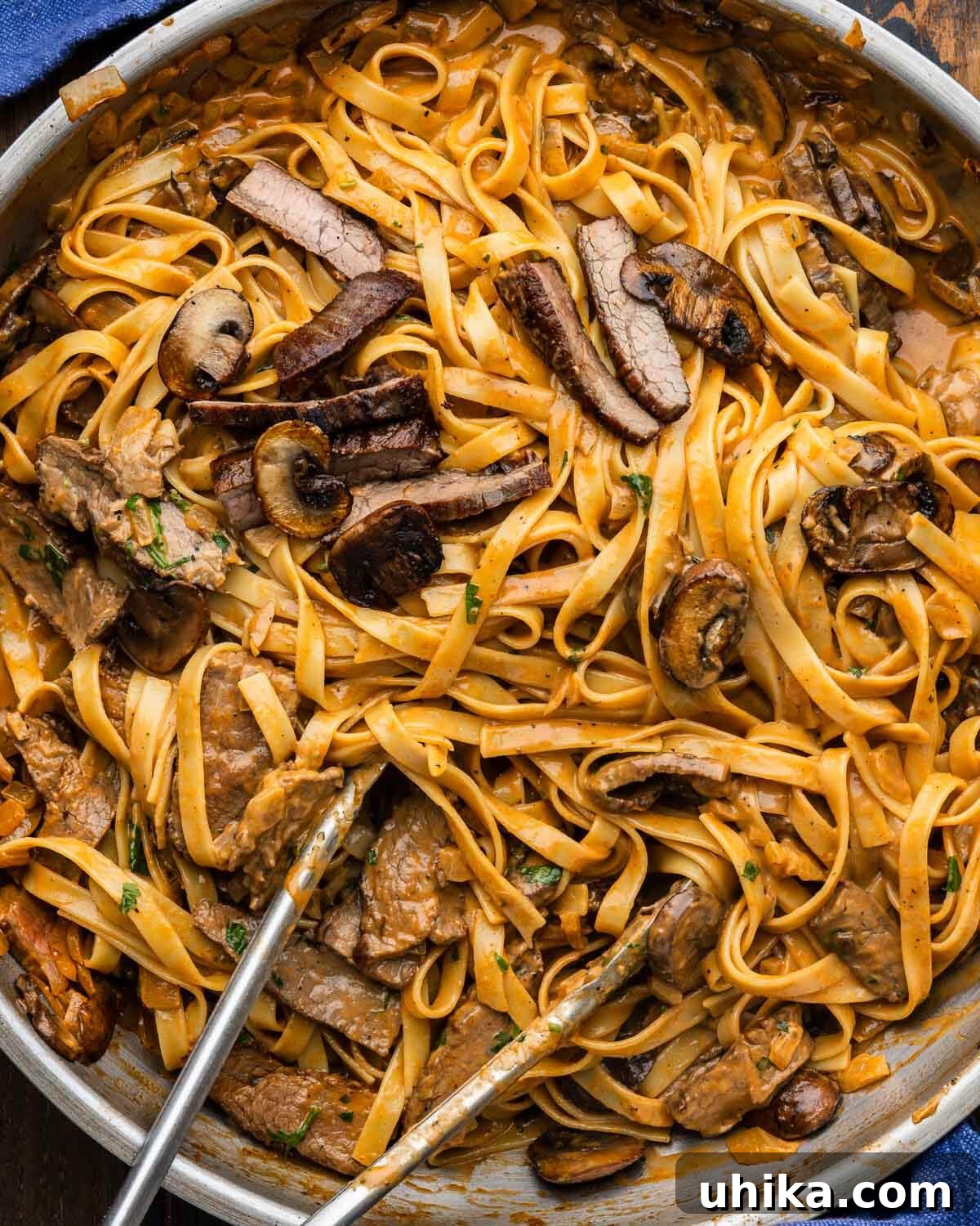 Large pan with bourbon steak and mushroom pasta, garnished with fresh parsley.