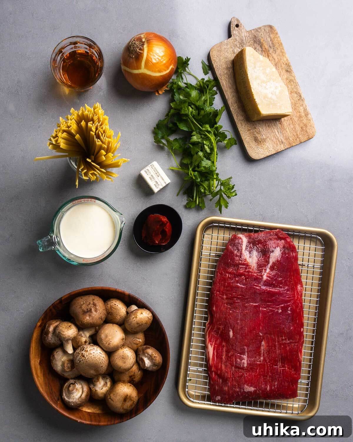 Ingredients shown: bourbon, onion, fresh parsley, Parmesan block, fettuccine, butter, heavy cream, tomato paste, cremini mushrooms, and flank steak.