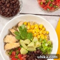 An overhead view of Southwest chicken quinoa bowl with black beans, corn, avocado, diced tomatoes, green onions, and fresh cilantro.