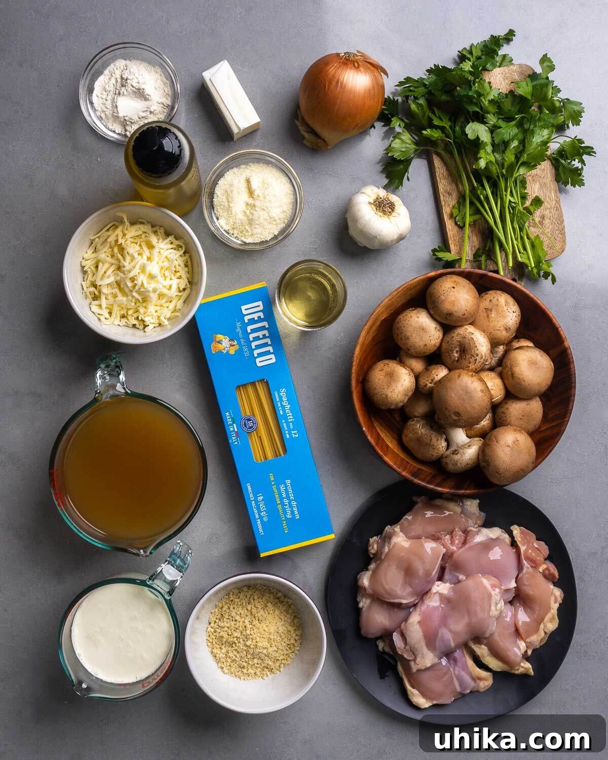 Creamy Comfort Chicken Tetrazzini 4 A flat lay of all the essential ingredients for Chicken Tetrazzini, including boneless skinless chicken thighs, spaghetti, cremini mushrooms, olive oil, butter, onions, garlic, all-purpose flour, dry white wine, low-sodium chicken stock, heavy cream, mozzarella cheese, Parmesan cheese, fresh parsley, salt, pepper, and panko breadcrumbs.