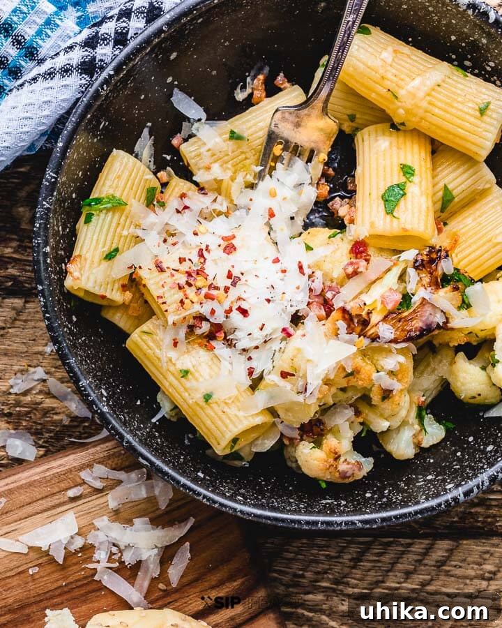 Rigatoni with Cauliflower and Bacon Pasta - Easy Weeknight Dinner Recipe A bowl of Rigatoni with cauliflower and bacon, garnished with fresh parsley, on a rustic wooden table, ready to be enjoyed.