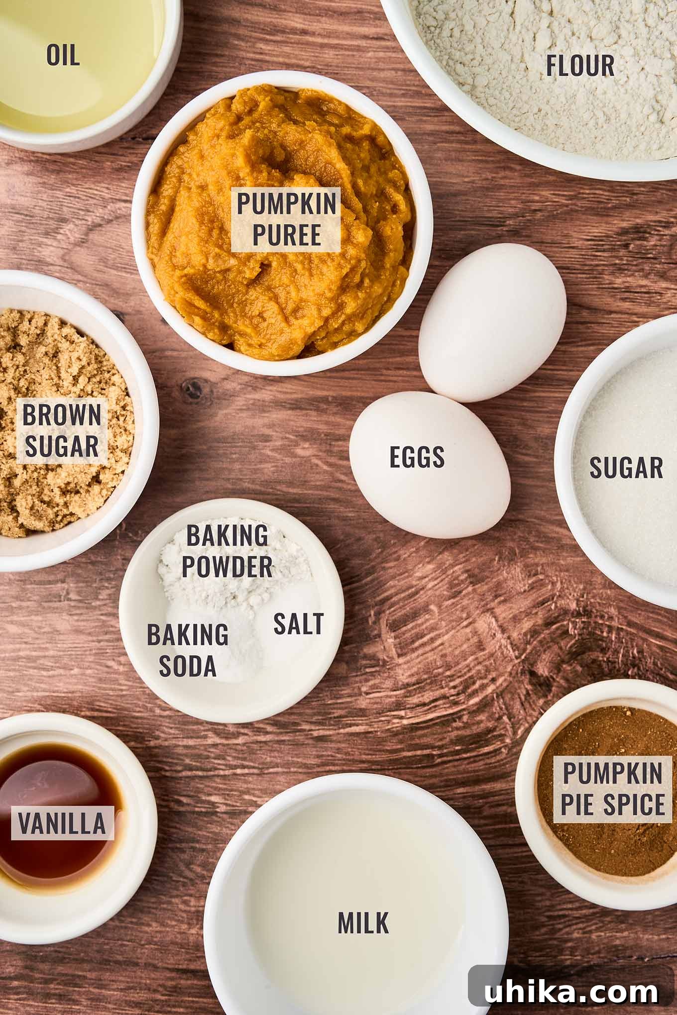 Cozy Pumpkin Spice Bites 3 A labeled, overhead view of pumpkin spice muffin ingredients; pumpkin puree, flour, eggs, brown sugar, sugar, pumpkin pie spice, milk, vanilla, and oil.