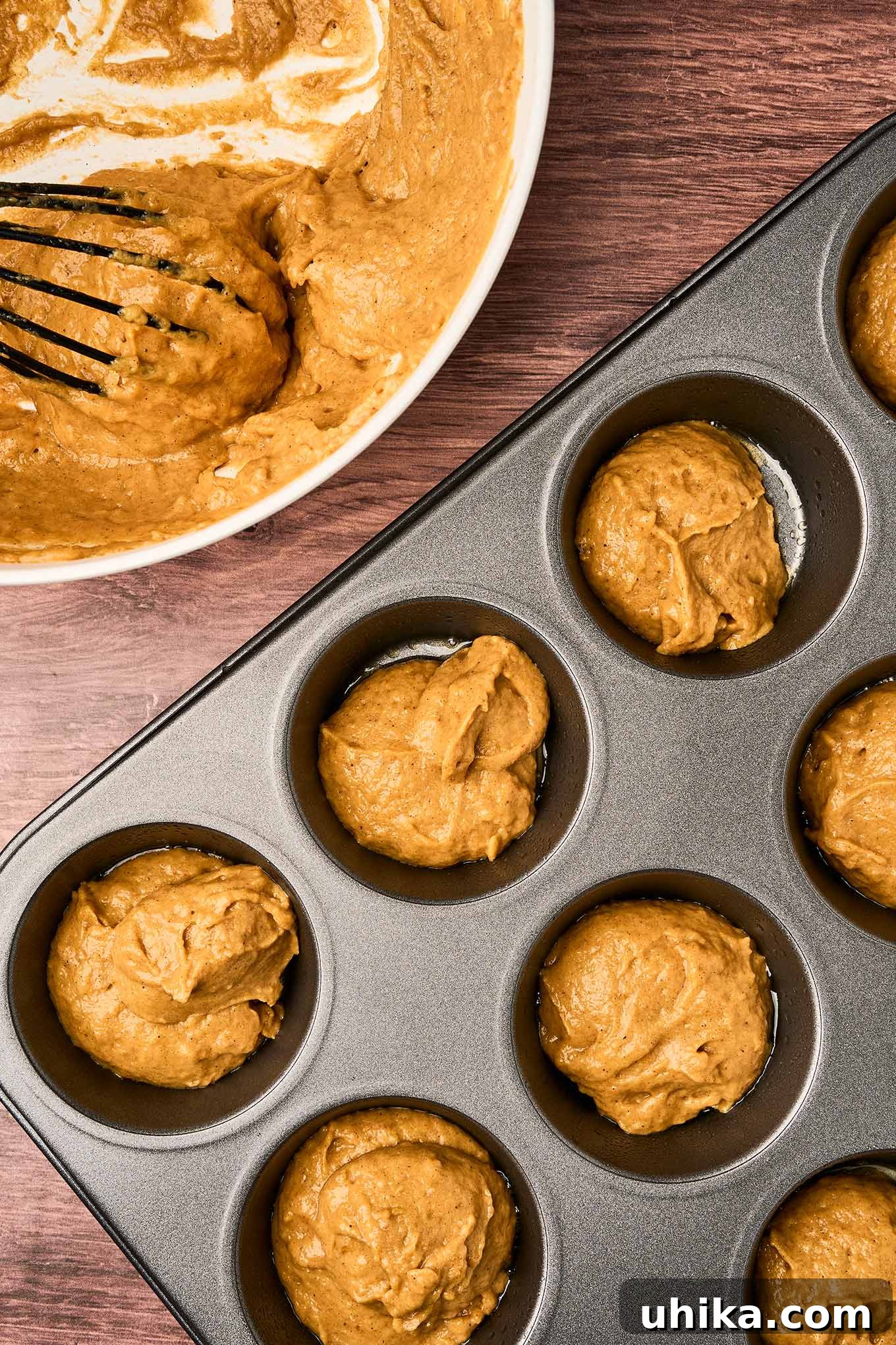 Cozy Pumpkin Spice Bites 5 Pumpkin spice muffin batter spooned into a muffin tin and ready for baking, a bowl with more batter and whisk in the background.