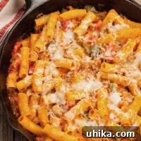 Skillet baked ziti with sausage and bell peppers, topped with melted cheese and served in a cast iron pan on a rustic wooden table.