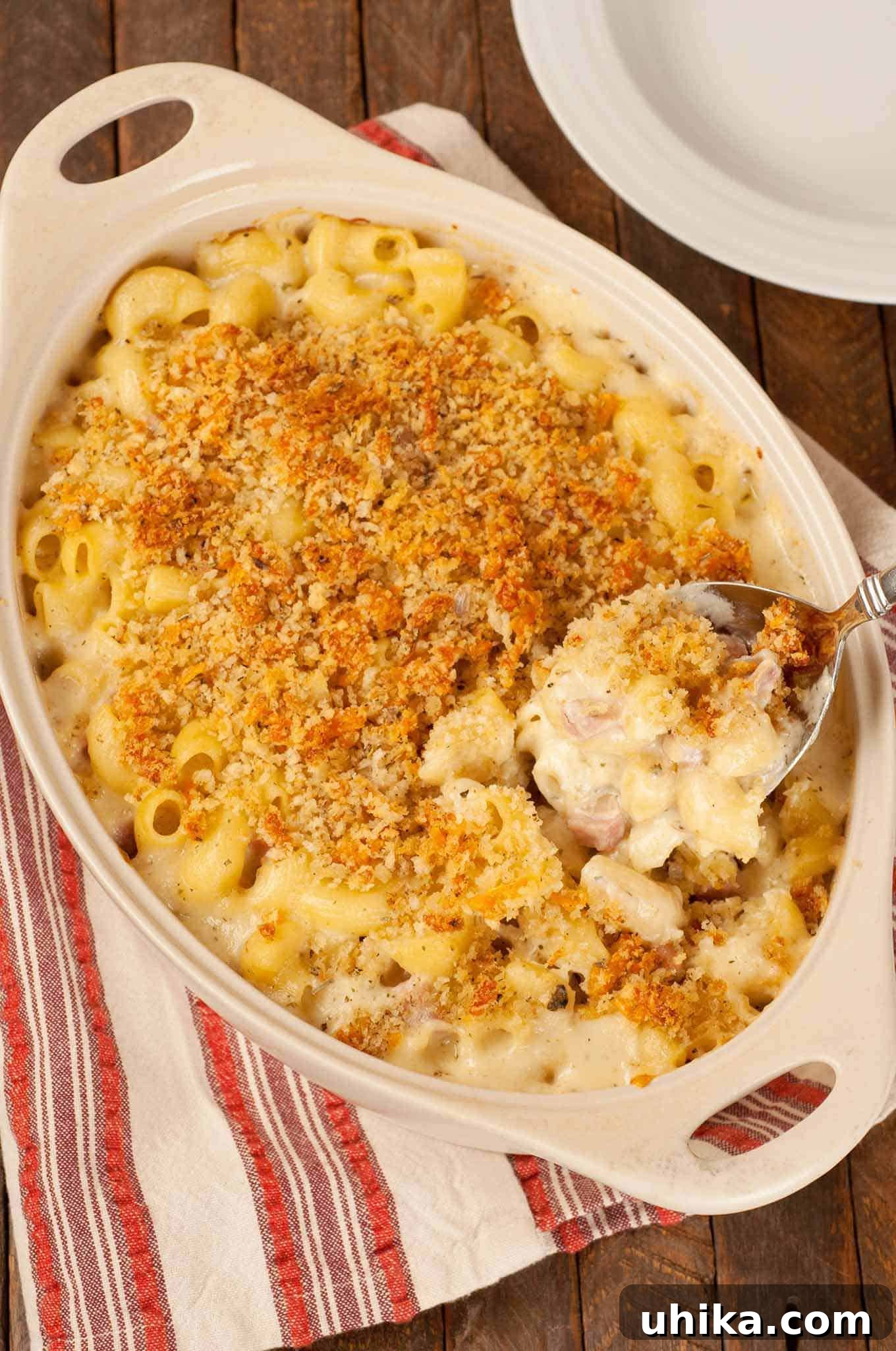Classic French Macaroni Gratin 2 A golden-brown French-inspired macaroni and cheese casserole, generously topped with toasted panko breadcrumbs, with a serving spoon scooping out a creamy portion. The rich, cheesy interior is visible, showcasing the blend of French cheeses and diced ham.