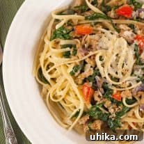 A bowl of linguine pasta tossed with crumbled sausage, wilted spinach, red bell peppers, and shredded Parmesan cheese.