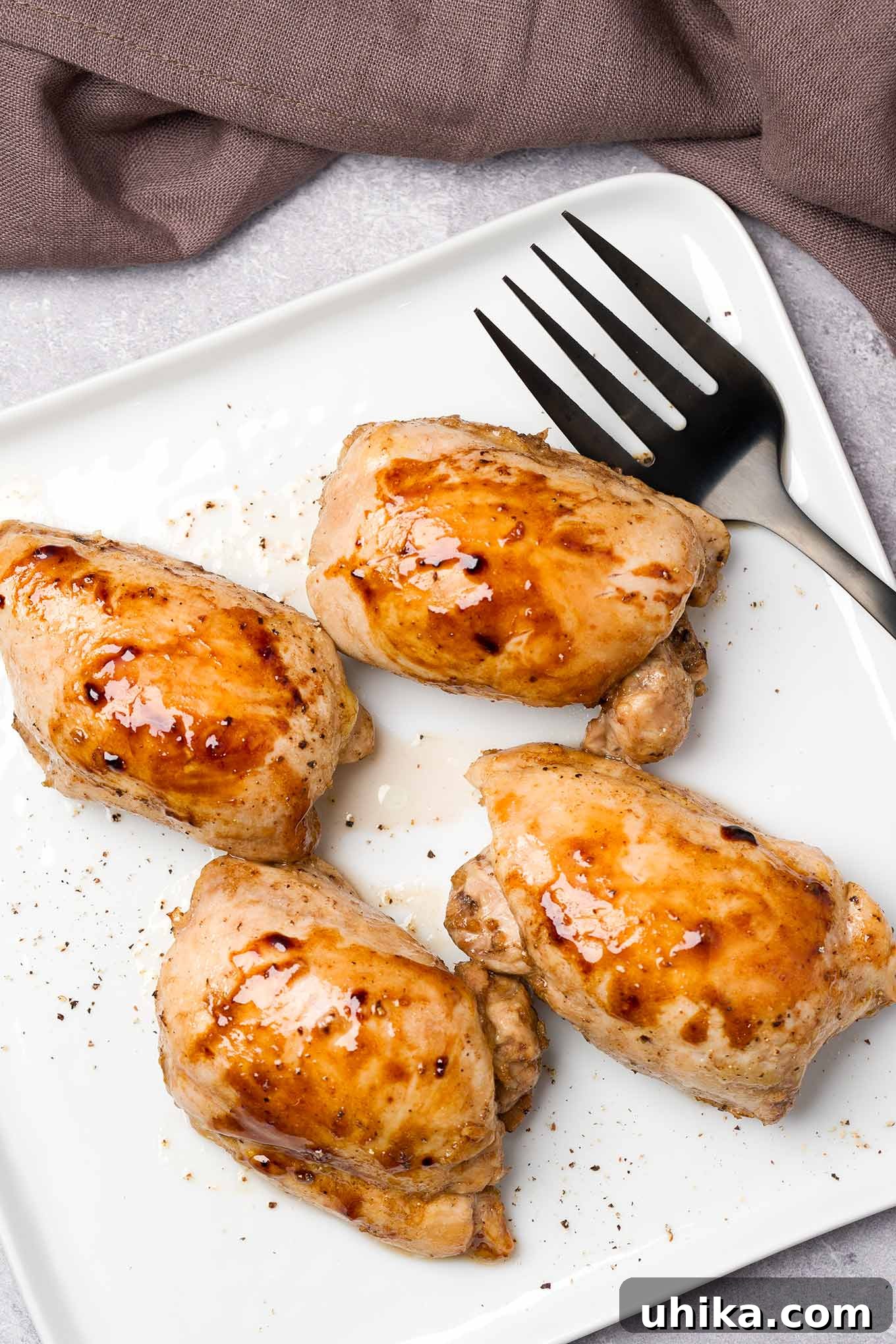 Succulent Oven-Roasted Boneless Chicken Thighs 2 A square serving plate containing four roasted boneless, skinless chicken thighs, glazed with honey and balsamic vinegar.