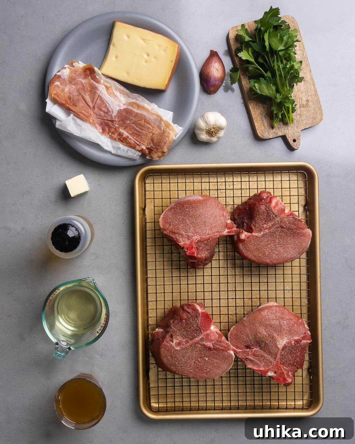 Creamy Fontina and Savory Prosciutto Stuffed Pork Chops 4 A flat lay of all ingredients for stuffed pork chops: fontina cheese, prosciutto, shallot, garlic, fresh parsley, butter, olive oil, thick pork chops, white wine, and chicken stock.