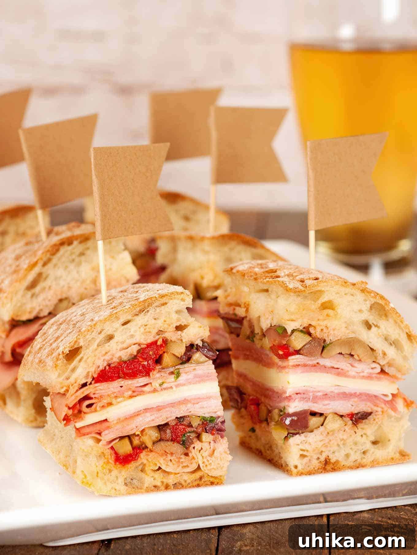 Big Easy Muffaletta Bites 2 Party-sized portions of muffaletta sandwiches stacked with layers of deli meats, cheese, and olive salad on crusty bread, each topped with a small flag toothpick, arranged beautifully for a gathering.