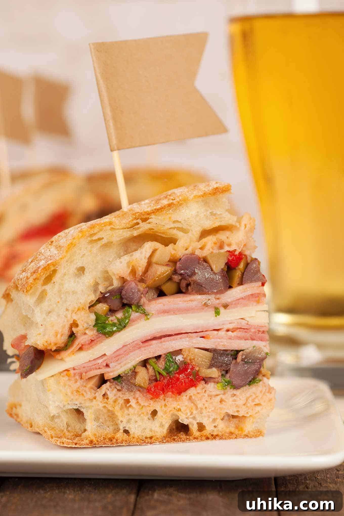 Big Easy Muffaletta Bites 3 A close-up view of a perfectly cut muffaletta sandwich, showcasing its vibrant layers of deli meats, rich Provolone cheese, and abundant olive salad nestled within crusty ciabatta bread.