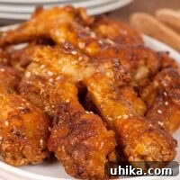 Crispy oven-fried chicken wing drumettes coated in a golden glaze and sprinkled with sesame seeds, served on a white plate.