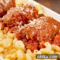 Close up photo of slow-cooked Italian beef braciole served with tomato and red wine sauce over pasta.