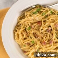 One-pot spaghetti alla carbonara served in a white bowl, topped with crispy bacon, parsley, and cracked black pepper.