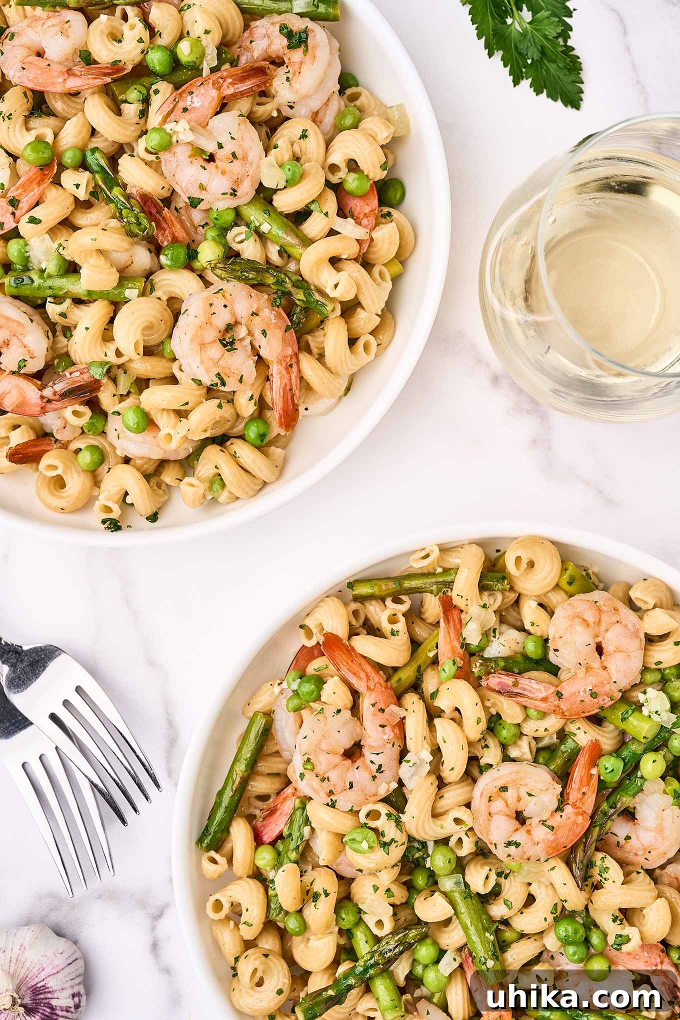 Vibrant Shrimp Primavera 2 An overhead view of two bowls of vibrant shrimp pasta primavera on a marble surface, garnished with fresh parsley and served with white wine.