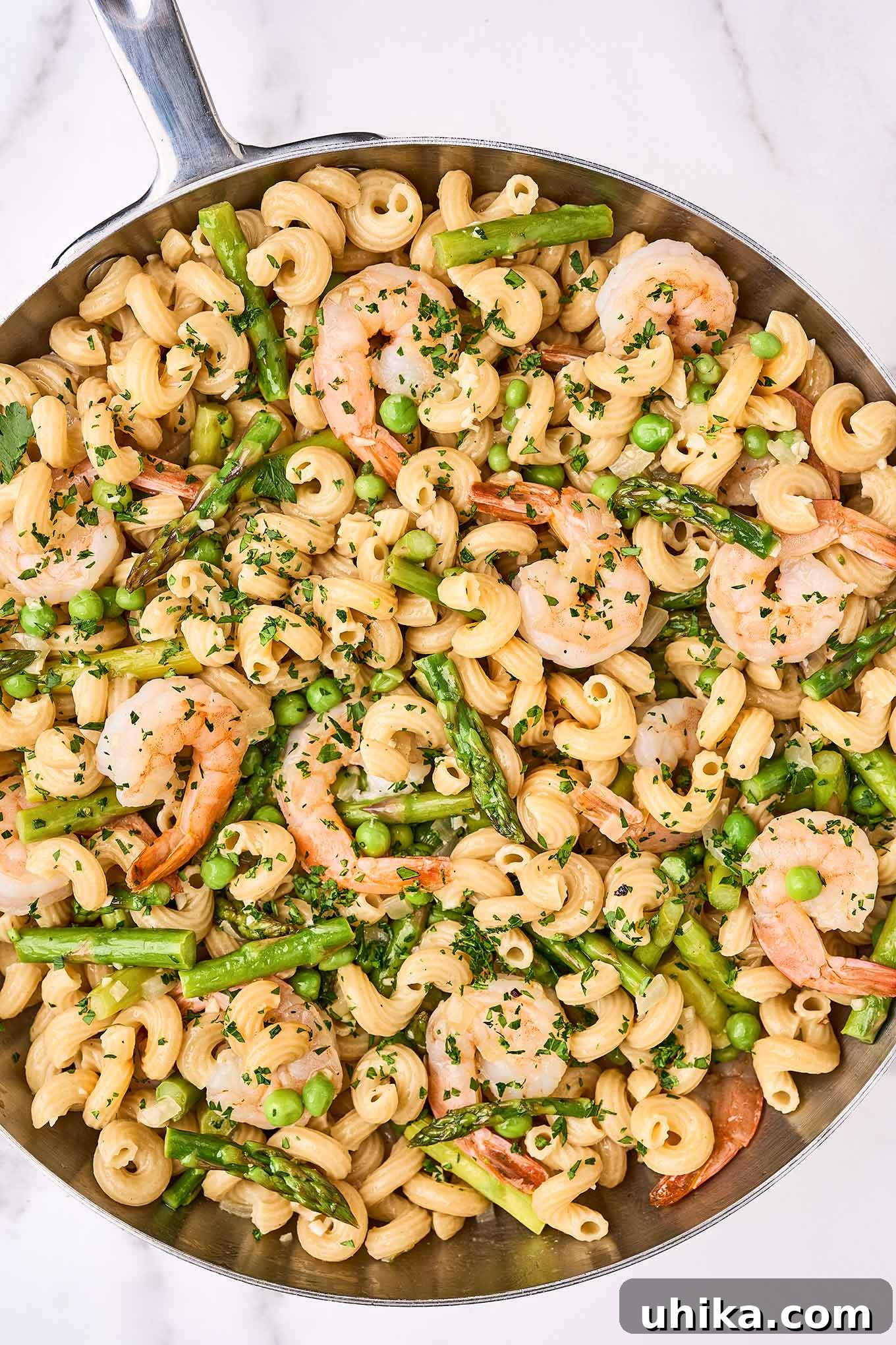 Vibrant Shrimp Primavera 7 A stainless steel sauté pan filled with corkscrew pasta, sautéed shrimp, asparagus, peas, and fresh parsley, coated in a light white wine sauce.