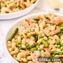A close view of a bowl of pasta primavera with shrimp, another serving and a glass of wine to the rear.