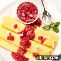 Three Hungarian crepes filled with sweetened cottage cheese, topped with raspberry sauce and powdered sugar, garnished with fresh mint.
