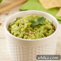 Chunky homemade guacamole in a white ramekin, garnished with a sprig of cilantro, with tortilla chips and lime in the background.