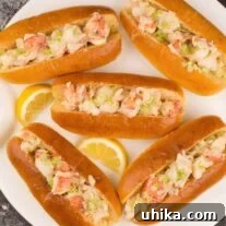 Five New England–style lobster rolls on a white plate, garnished with lemon slices.