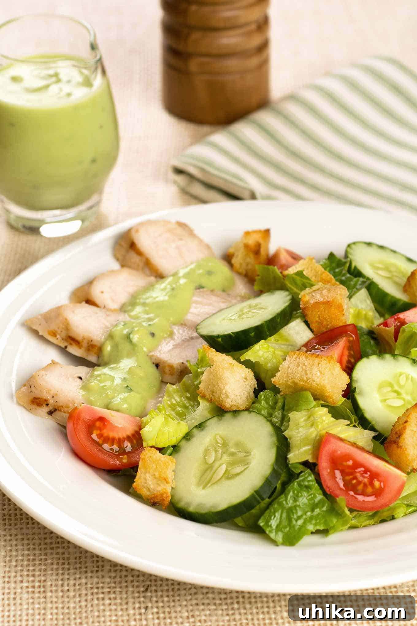 Smoky Turkey Salad with Creamy Avocado 2 Slices of grilled turkey tenderloins on a salad of crisp lettuce, juicy tomatoes, cool cucumbers, crunchy croutons, and a vibrant, creamy avocado dressing. A pitcher of extra dressing is visible in the background.