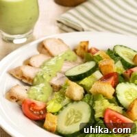 Slices of grilled turkey tenderloins on a salad of lettuce, tomatoes, cucumbers, croutons, and a creamy avocado dressing, more dressing in a pitcher in the background.