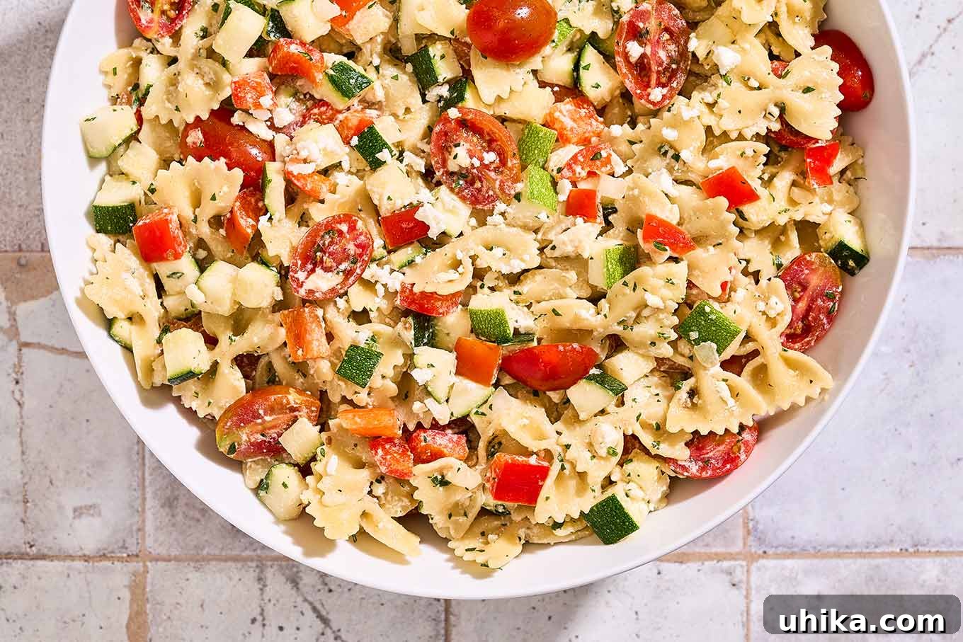 Zesty Lemon Cream Pasta Salad 7 A serving bowl filled with creamy pasta salad made with farfalle, zucchini, red bell pepper, grape tomatoes, feta cheese, parsley, and lemon dressing.