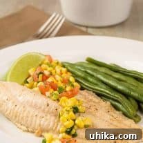 A plate of broiled catfish filet topped with fresh corn salsa, steamed green beans, and a lime wedge.