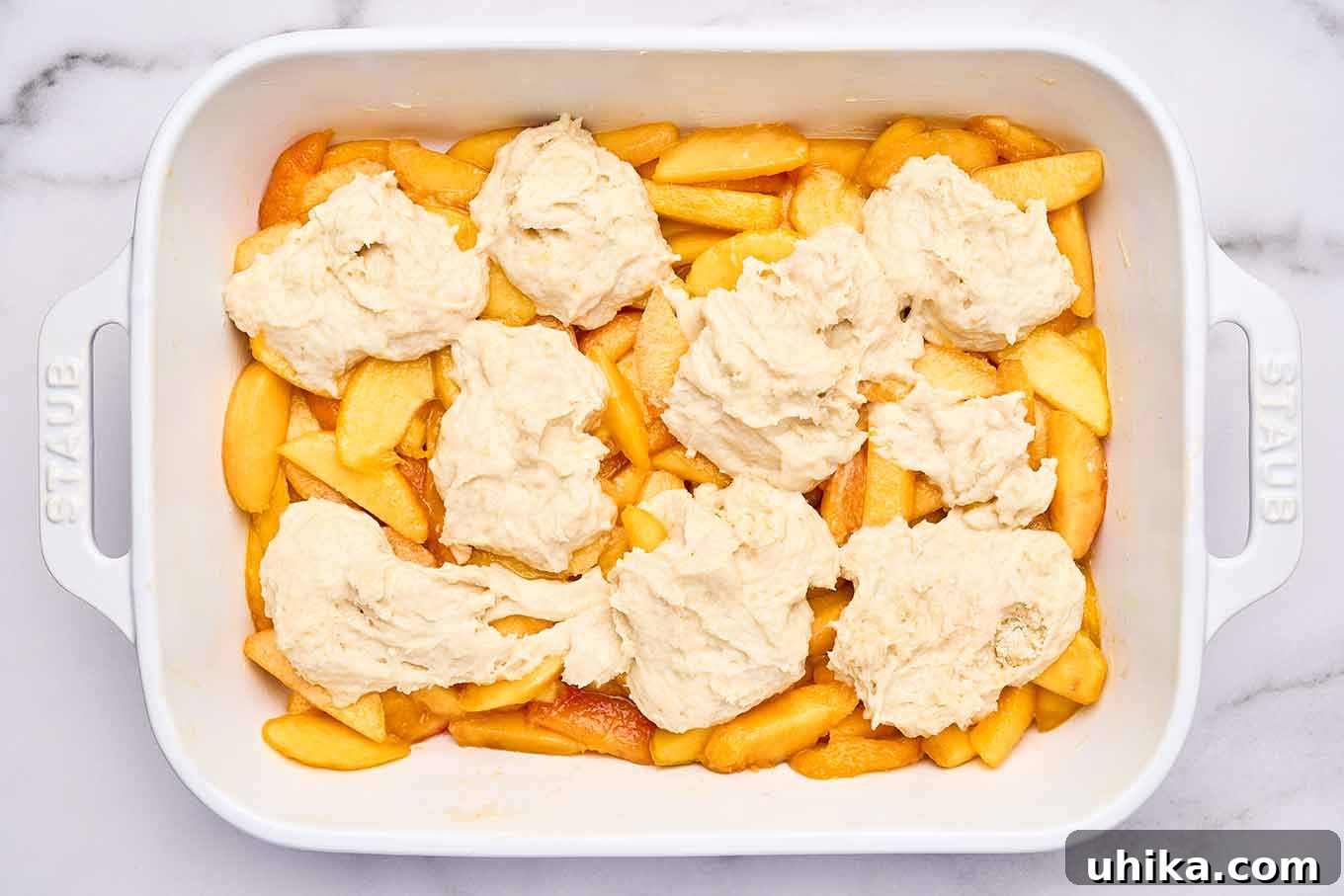 Summertime Fresh Peach Cobbler 6 An overhead view of peach cobbler ready for the oven showing an oblong baking dish filled with sliced peaches topped with biscuit dough.