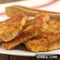 Breaded, shallow-fried pork chops stacked on a serving plate with a pair of wooden serving tongs.